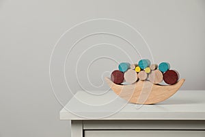 Wooden balance toy on chest of drawers near light grey wall, space for text. Children's development