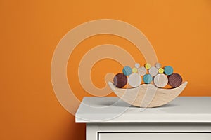 Wooden balance toy on white chest of drawers near orange wall, space for text. Children's development