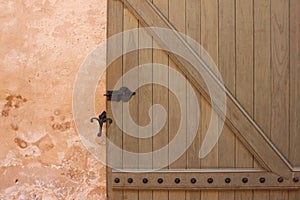Wooden barn door. Wooden plank door with forged metal parts over old plaster wall
