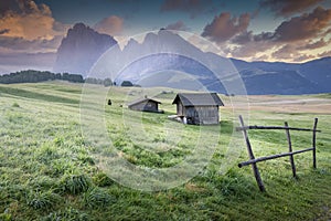 Wooden barn in a grassy field with high rocky mountains in the background