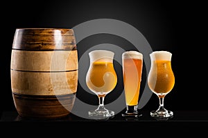 Wooden barrel with Different glasses and cups with beer, on a dark table, dark background and copy space