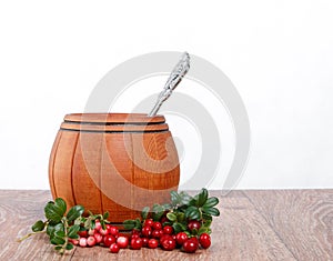 Wooden barrel with spoon and lingonberries on a white background
