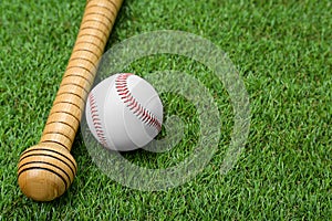 Wooden baseball bat and ball on green grass, closeup.