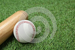 Wooden baseball bat and ball on green grass, closeup. Space for text