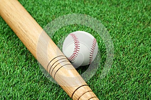 Wooden baseball bat and ball on green grass, closeup. Sports equipment