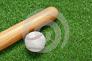 Wooden baseball bat and ball on green grass, closeup. Sports equipment