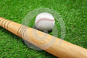 Wooden baseball bat and ball on green grass, closeup. Sports equipment