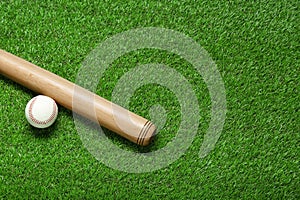 Wooden baseball bat and ball on green grass, flat lay. Space for text