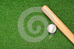 Wooden baseball bat and ball on green grass, flat lay. Space for text