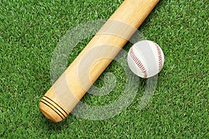 Wooden baseball bat and ball on green grass, flat lay. Sports equipment
