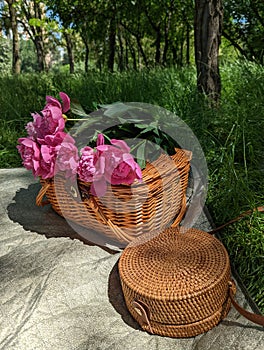 Wooden basket and bag with flowers on summer picnic with green grass on background