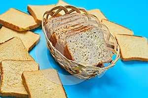 Wooden basket full of square pieces of bread with seeds and vanilla for toast lies on blue table on kitchen