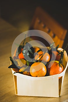 Wooden basket, packing, box with ripe raw oranges, mandarines at rustic kitchen.