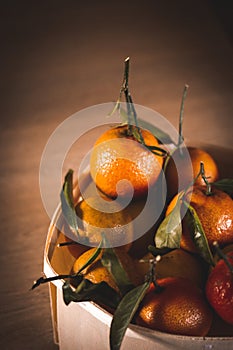 Wooden basket, packing, box with ripe raw oranges, mandarines at rustic kitchen.
