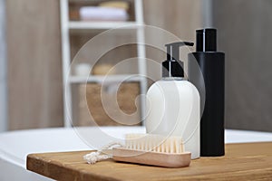 Wooden bath tray with bottles of shower gels and brush on tub indoors, space for text