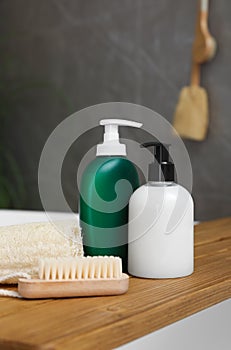 Wooden bath tray with bottles of shower gels, loofah and brush on tub indoors