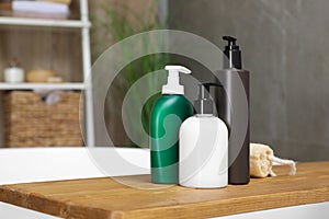 Wooden bath tray with bottles of shower gels and loofah on tub indoors, space for text