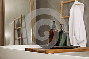 Wooden bath tray with bottles of shower gels on tub indoors, space for text