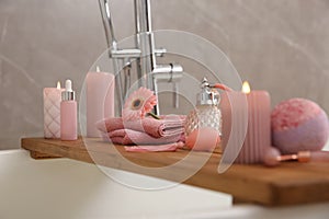 Wooden bath tray with candles and personal care products on tub, closeup