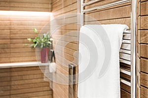 Wooden bathroom interior with heated towel rail and white towel on it