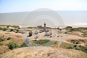 Wooden Beacon against the background of the sea. The small village surrounded with a fence. Green trees and footpaths