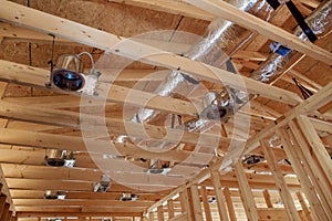 Wooden beamed ceiling in new home is being equipped with a central HVAC system an electric spotlight floodlight.