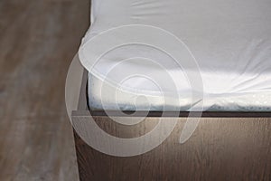 Wooden bed with a high mattress and a covered white mattress cover