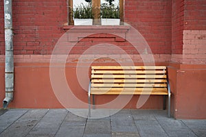 Wooden bench against a brick wall of a house with a window