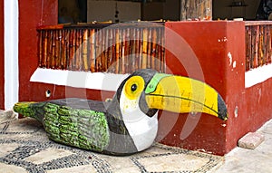 Wooden bench carved into a toucan bird shape sitting on mosiac sidewalk against bambo and stucco wall in Mexico