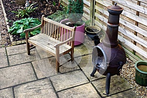Wooden bench, chiminea and various plants, some in pots, in a sm
