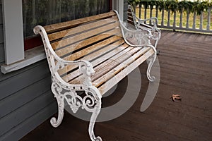 Wooden bench with a decorative ornate metal legs and armrests. Garden white bench with a handcrafted wrought iron arm