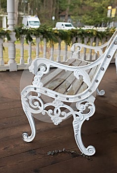 Wooden bench with a decorative ornate metal legs and armrests. Garden white bench with a handcrafted wrought iron arm