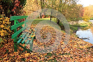 Wooden bench in forest near lake on background of colorful autumn leaves.