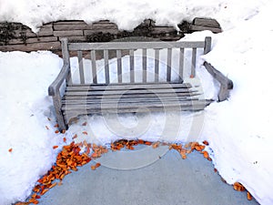 Wooden Bench At Park Covered in Winter Snow with Leaves