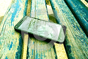 On a wooden bench in the Park is a smartphone with a broken screen