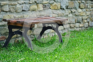 Wooden bench placed on the lawn with a river stone background.