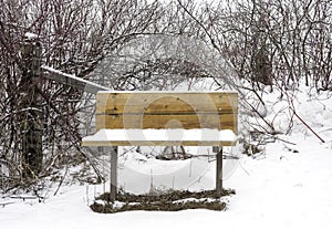 Wooden bench seat in wilderness and rural area covered with winter snow