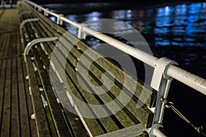 Wooden bench seating on the pier captured at night, and the calm sea in the background