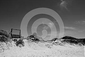 Wooden bench swing on deserted sand dune