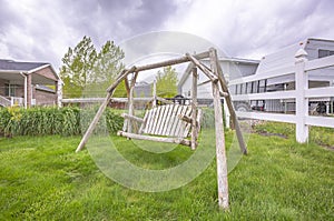 Wooden bench swing at the lush grassy yard of a home with white picket fence