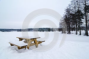 Wooden bench and table covered of snow in a snowy forest landscape. Frozen lake. photo