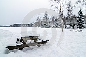 Wooden bench and table covered of snow in a snowy forest landscape panorama photo