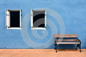 Wooden bench and two windows with the blue wall