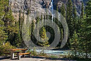 Wooden bench by the Yoho River over Takakkaw Falls in a summer day. Yoho National Park, Canadian Rockies.