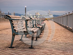 Wooden benches aligned in line on the pier with boats at the background