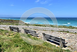 Wooden benches on a beach promenade with turquoise sea, waves and blue sky. Viveiro, Lugo, Galicia, Spain.