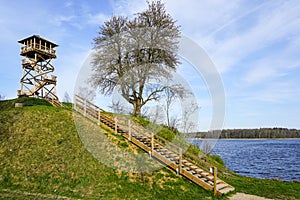 A wooden bird watching tower on top of a hill by the lake