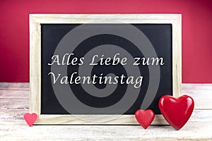 Wooden blackboard with red hearts and written sentence in German Alles Liebe zum Valentinstag, which means happy valentine photo