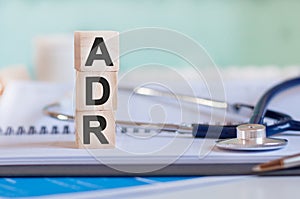 Wooden block form the word ADR with stethoscope on the doctor`s desktop. Medical concept