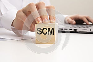 a wooden block with the letters SCM written on it on a white background. SCM - short for Supply Chain Management